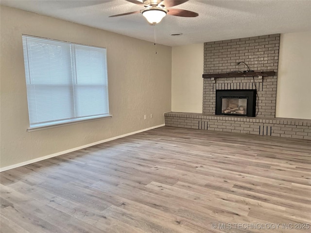 unfurnished living room with ceiling fan, a fireplace, a textured ceiling, and light wood-type flooring