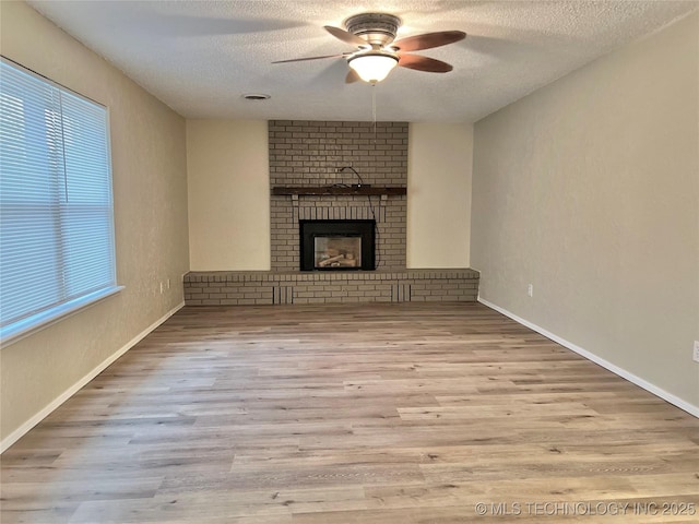 unfurnished living room with ceiling fan, a fireplace, a textured ceiling, and light wood-type flooring