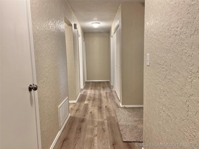 hall with a textured ceiling and light wood-type flooring