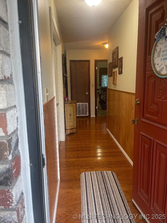 hallway with dark hardwood / wood-style floors, a textured ceiling, and wood walls