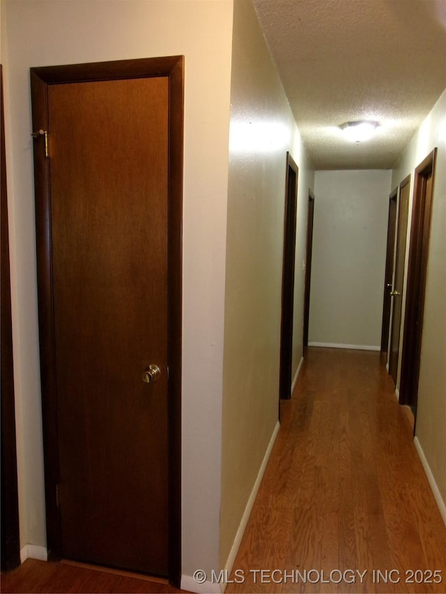 hallway featuring a textured ceiling, baseboards, and wood finished floors