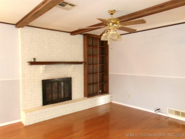 unfurnished living room featuring a brick fireplace, visible vents, beamed ceiling, and wood finished floors