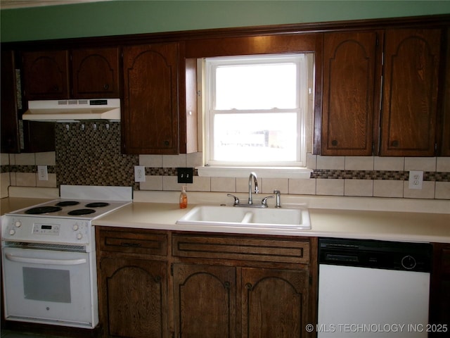 kitchen with under cabinet range hood, white appliances, a sink, light countertops, and backsplash