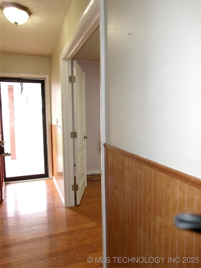 corridor featuring a textured ceiling, wainscoting, wood finished floors, and wooden walls