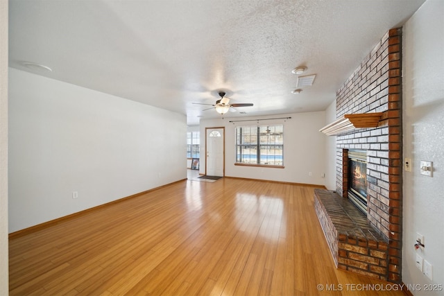 unfurnished living room featuring light hardwood / wood-style flooring, ceiling fan, a fireplace, and a textured ceiling