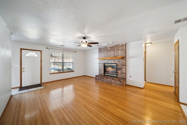 unfurnished living room featuring ceiling fan, a fireplace, light hardwood / wood-style floors, and a textured ceiling