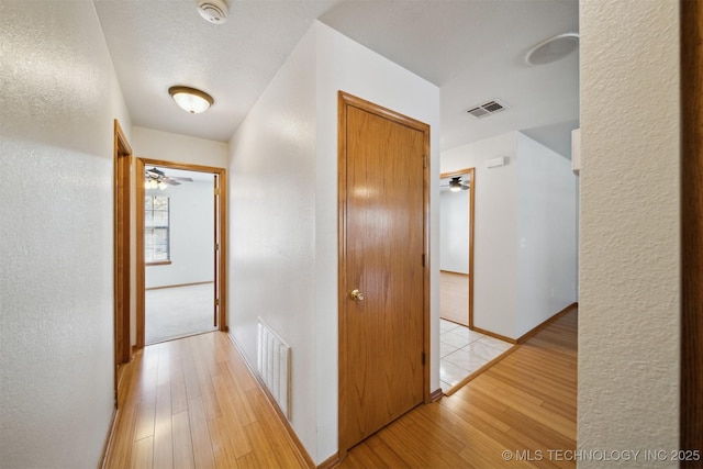 hall with a textured ceiling and light wood-type flooring