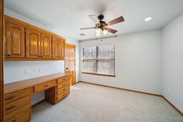 unfurnished office featuring light carpet, built in desk, and ceiling fan