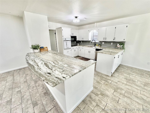 kitchen featuring sink, kitchen peninsula, light stone countertops, decorative backsplash, and white cabinets