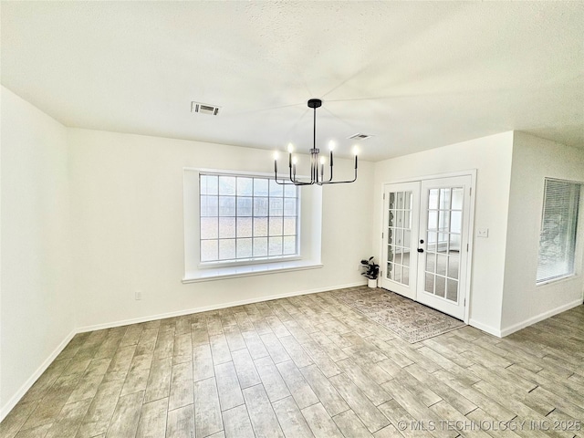 unfurnished dining area with a notable chandelier, light wood-type flooring, and french doors