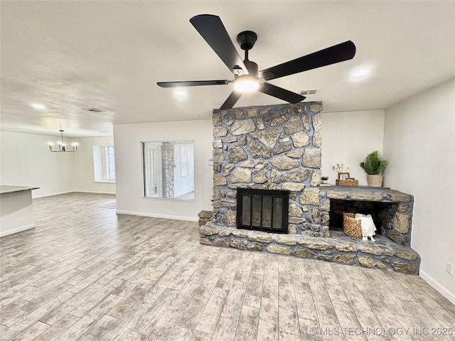 living room with hardwood / wood-style floors, a stone fireplace, and ceiling fan with notable chandelier