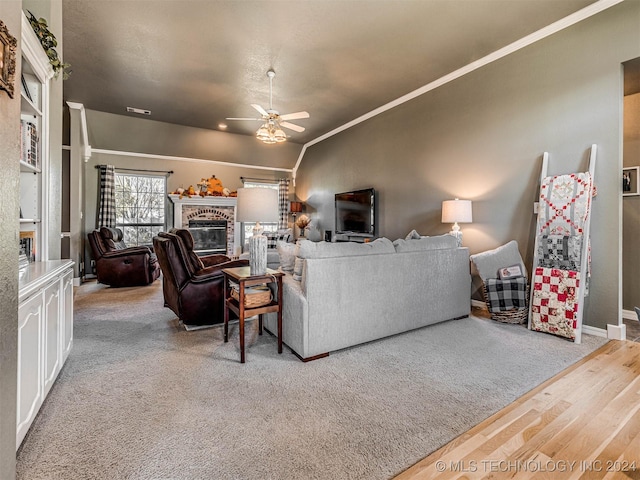 living room featuring vaulted ceiling, ornamental molding, hardwood / wood-style flooring, ceiling fan, and a fireplace