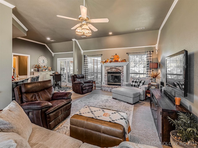 carpeted living room with ornamental molding, vaulted ceiling, ceiling fan, and a fireplace