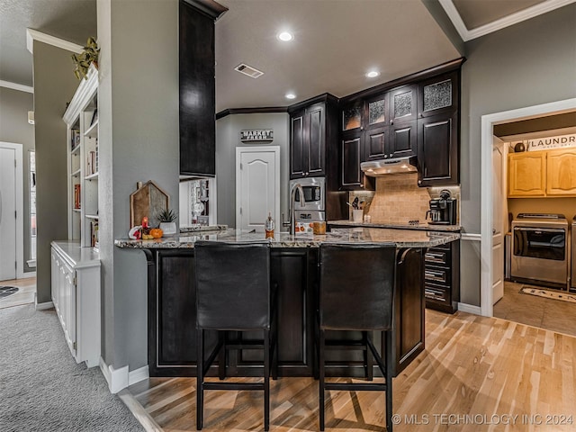 kitchen featuring stainless steel microwave, a kitchen breakfast bar, ornamental molding, kitchen peninsula, and light stone countertops