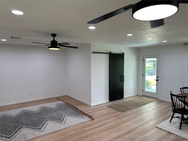 foyer entrance with ceiling fan, a barn door, light hardwood / wood-style floors, and a textured ceiling