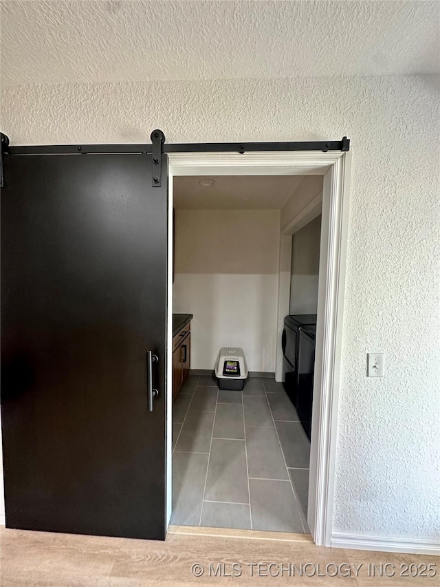 hall featuring tile patterned flooring, washing machine and dryer, a barn door, and a textured ceiling