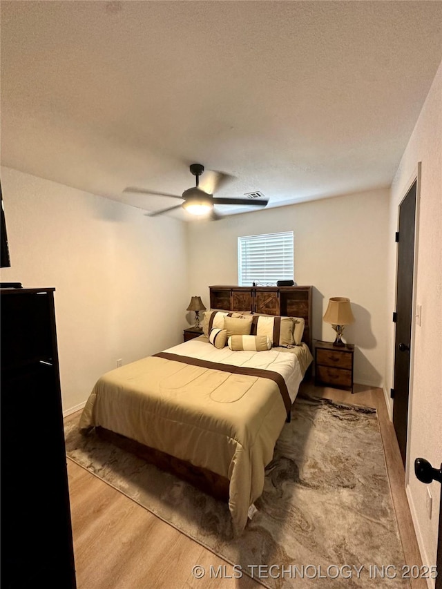 bedroom with a textured ceiling, light hardwood / wood-style floors, and ceiling fan