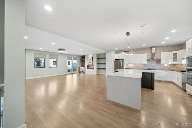 kitchen with a kitchen island, appliances with stainless steel finishes, pendant lighting, white cabinetry, and wall chimney range hood