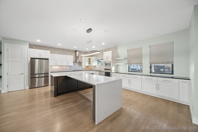 kitchen with a center island, appliances with stainless steel finishes, light wood-style floors, white cabinetry, and wall chimney range hood