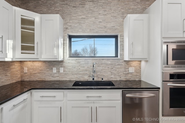 kitchen with sink, white cabinetry, stainless steel appliances, decorative backsplash, and dark stone counters