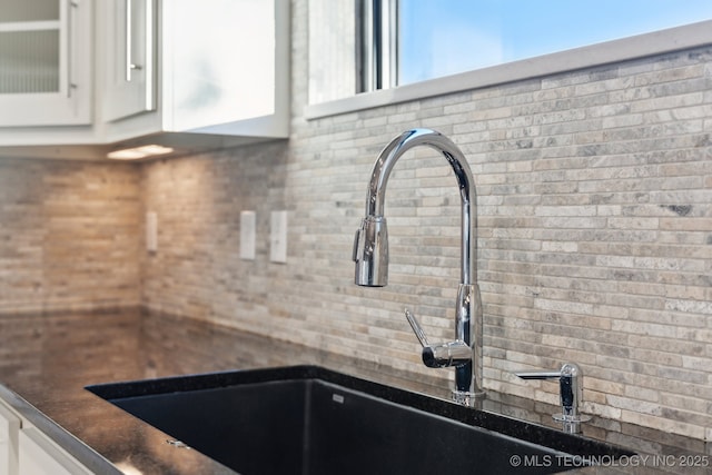 interior details with dark countertops, a sink, glass insert cabinets, and white cabinets