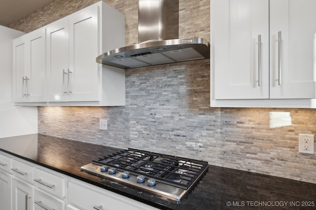 kitchen featuring white cabinets, wall chimney range hood, tasteful backsplash, dark countertops, and stainless steel gas stovetop