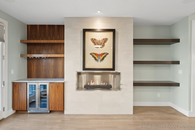 interior details featuring beverage cooler, a fireplace, wood finished floors, and baseboards