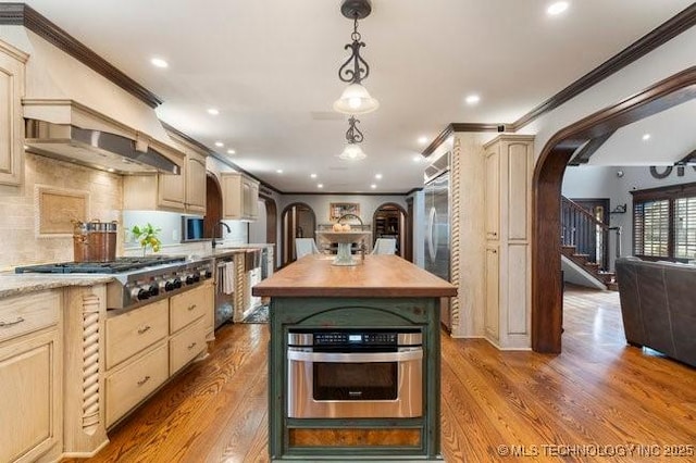 kitchen featuring appliances with stainless steel finishes, a kitchen island, wood counters, decorative light fixtures, and ornamental molding