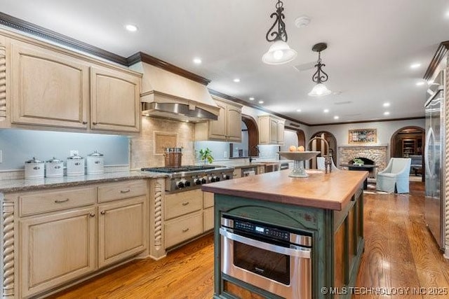 kitchen with appliances with stainless steel finishes, wooden counters, hanging light fixtures, a center island, and light hardwood / wood-style flooring