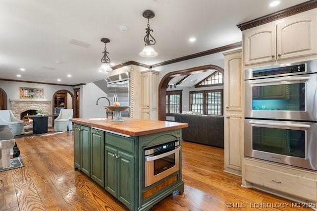 kitchen featuring green cabinetry, a kitchen island, pendant lighting, stainless steel double oven, and light hardwood / wood-style floors