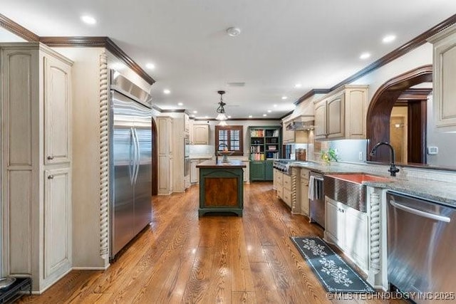 kitchen featuring crown molding, light hardwood / wood-style flooring, hanging light fixtures, stainless steel appliances, and dark stone counters