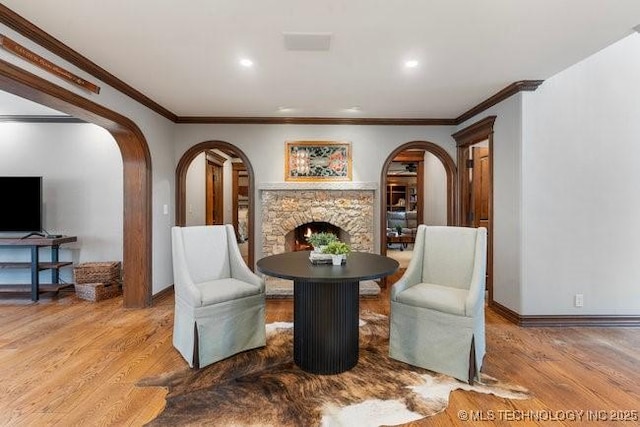 living area featuring a stone fireplace, ornamental molding, and light wood-type flooring