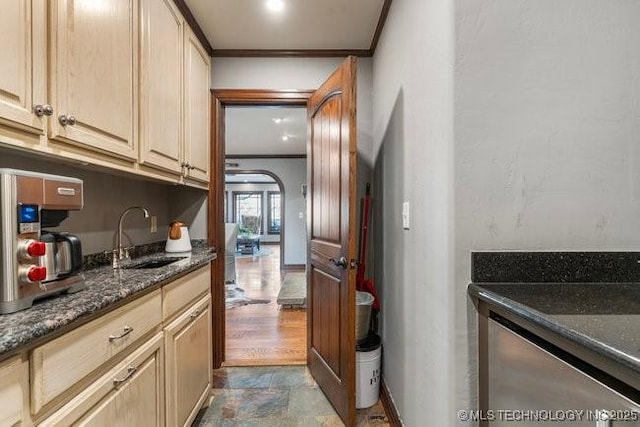 interior space with ornamental molding, sink, light brown cabinetry, and dark stone counters