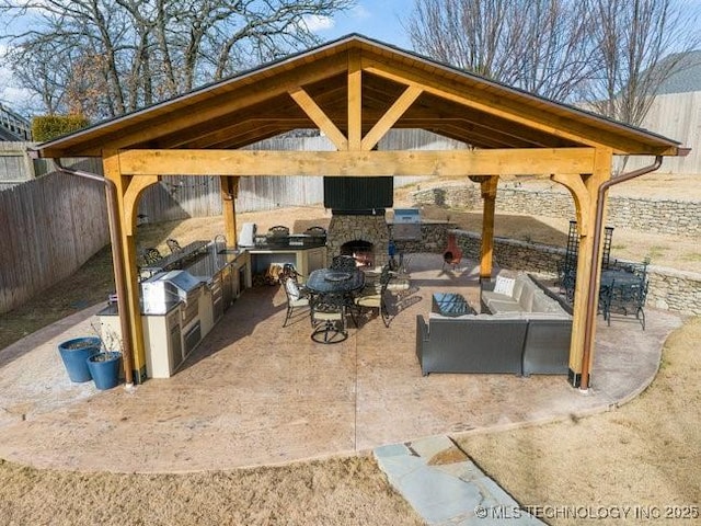 view of patio with exterior kitchen, a gazebo, and an outdoor stone fireplace