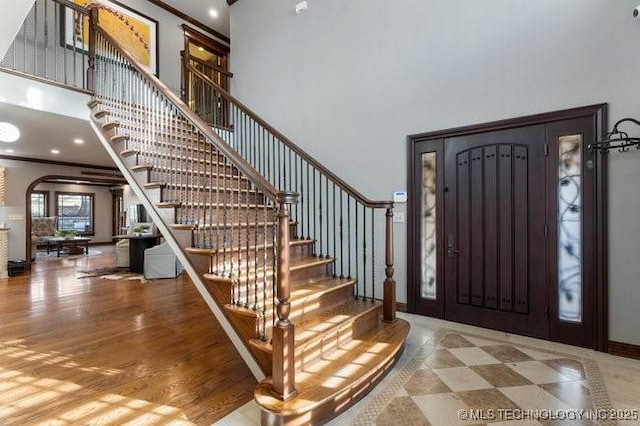 entrance foyer featuring crown molding, hardwood / wood-style floors, and a towering ceiling