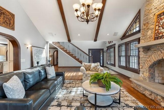 living room with high vaulted ceiling, beam ceiling, light hardwood / wood-style floors, and a stone fireplace