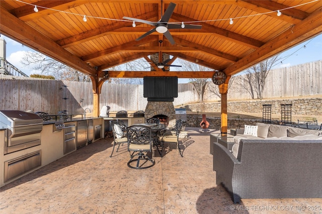 view of patio / terrace featuring an outdoor kitchen, a gazebo, grilling area, ceiling fan, and an outdoor stone fireplace