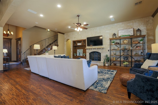 living room with dark hardwood / wood-style floors, a stone fireplace, and ceiling fan with notable chandelier