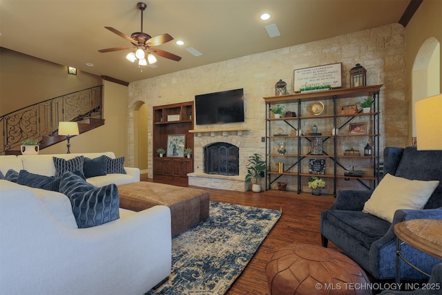 living room featuring dark hardwood / wood-style flooring, a stone fireplace, and ceiling fan