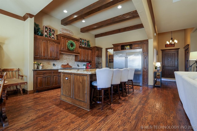 kitchen with a breakfast bar, stainless steel built in refrigerator, light stone countertops, an island with sink, and decorative backsplash