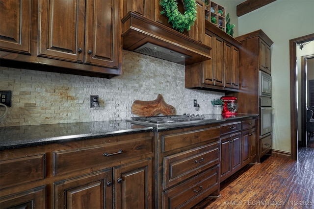 kitchen with tasteful backsplash, dark stone countertops, dark hardwood / wood-style flooring, custom exhaust hood, and stainless steel appliances