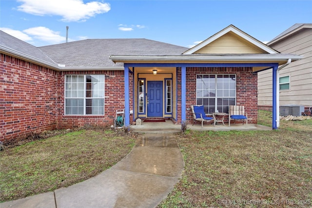 entrance to property with central AC unit, a yard, and covered porch