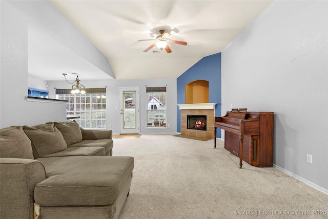 living room with a tile fireplace, vaulted ceiling, carpet flooring, and ceiling fan with notable chandelier