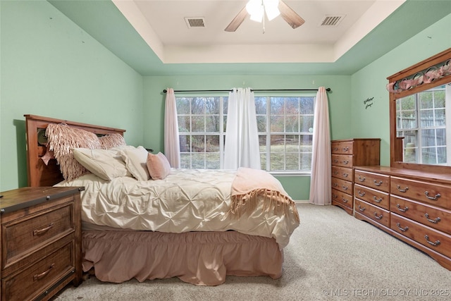 bedroom featuring a tray ceiling, light colored carpet, and ceiling fan