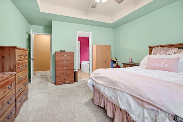 bedroom featuring light carpet, connected bathroom, a tray ceiling, and ceiling fan