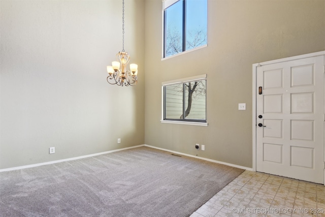 foyer featuring an inviting chandelier, a towering ceiling, a wealth of natural light, and light colored carpet