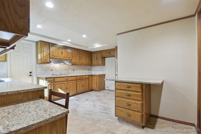 kitchen with light stone counters, backsplash, gas stovetop, and a raised ceiling