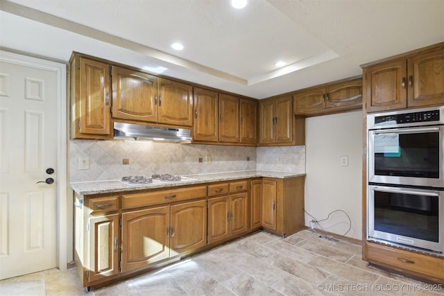 kitchen with white gas stovetop, a raised ceiling, double oven, and decorative backsplash