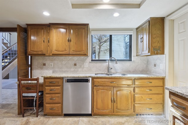 kitchen with light stone counters, stainless steel dishwasher, sink, and backsplash