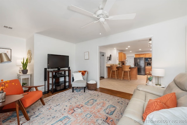 living room with ceiling fan, ornamental molding, and light wood-type flooring